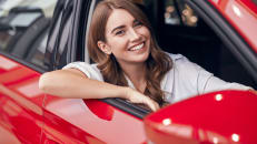 A woman sitting in a red car who knows about certain car insurance myths. 