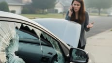 A woman talking on a cell phone with her car insurance company after items have been stolen from her car.