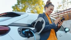 A woman charging her electric car and learning about car insurance for electric cars. 