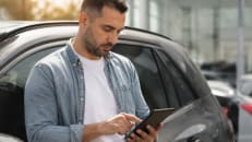 Man reviewing car loan payment options on his phone next to his vehicle.