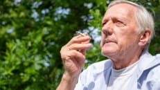 An older man smoking a cigarette in a park.