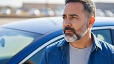 A man standing next to his car wondering about SR-22 insurance and whether he should get it.