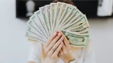 An image of a woman holding money in front of her face