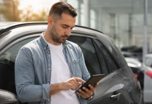 Man reviewing car loan payment options on his phone next to his vehicle.