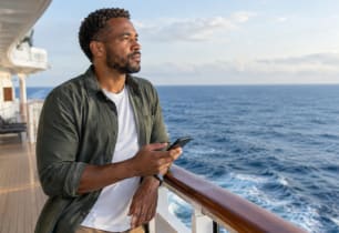 Man on a cruise ship deck researching cruise travel insurance options.