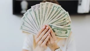 An image of a woman holding money in front of her face