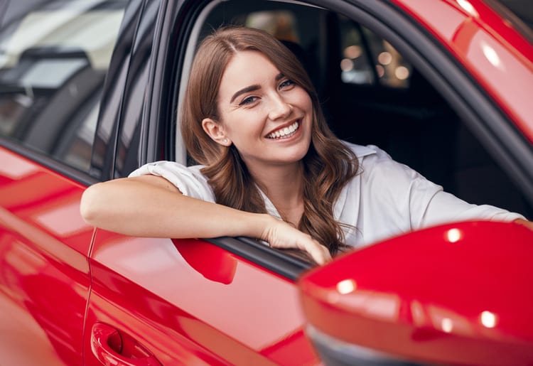 A woman sitting in a red car who knows about certain car insurance myths. 