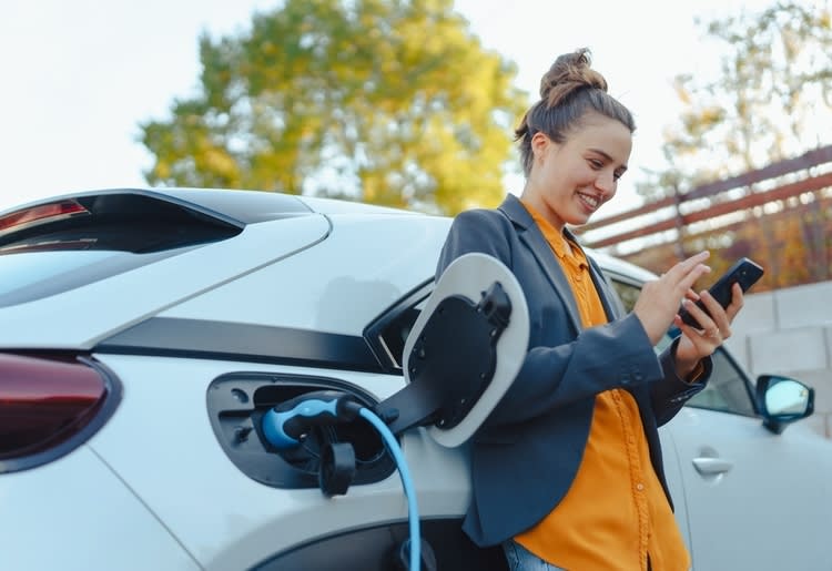 A woman charging her electric car and learning about car insurance for electric cars. 