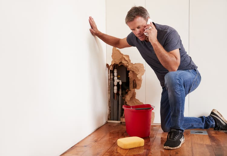 A man phoning his insurance company to deal with a burst water pipe due to floods in his high-risk area.