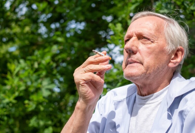 An older man smoking a cigarette in a park.